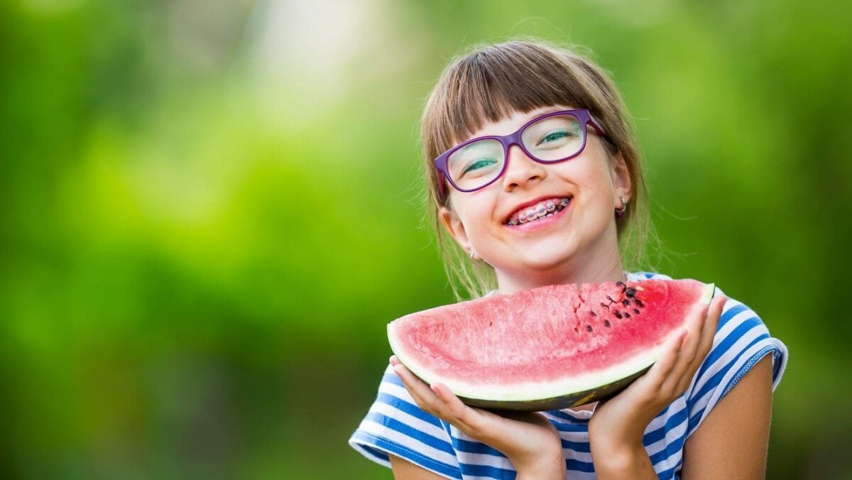 smiling girl with braces holding large slice of watermelon