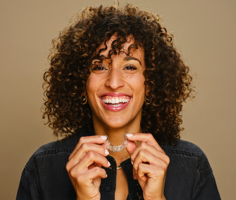 smiling woman with good teeth holding invisible aligners in hand